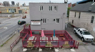 Outdoor patio at Ballyhoo Buffalo with picnic tables and umbrellas, ready for Stately Pole Barns’ custom covered deck transformation.