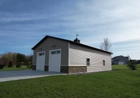 Angled view of post-frame garage with vertical siding, white overhead doors, and decorative cupola in Elma, NY.