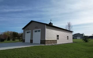 Angled view of post-frame garage with vertical siding, white overhead doors, and decorative cupola in Elma, NY.