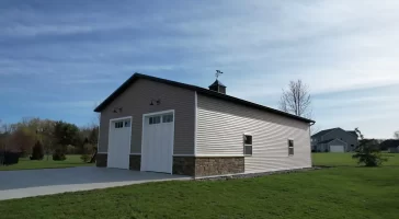 Angled view of post-frame garage with vertical siding, white overhead doors, and decorative cupola in Elma, NY.